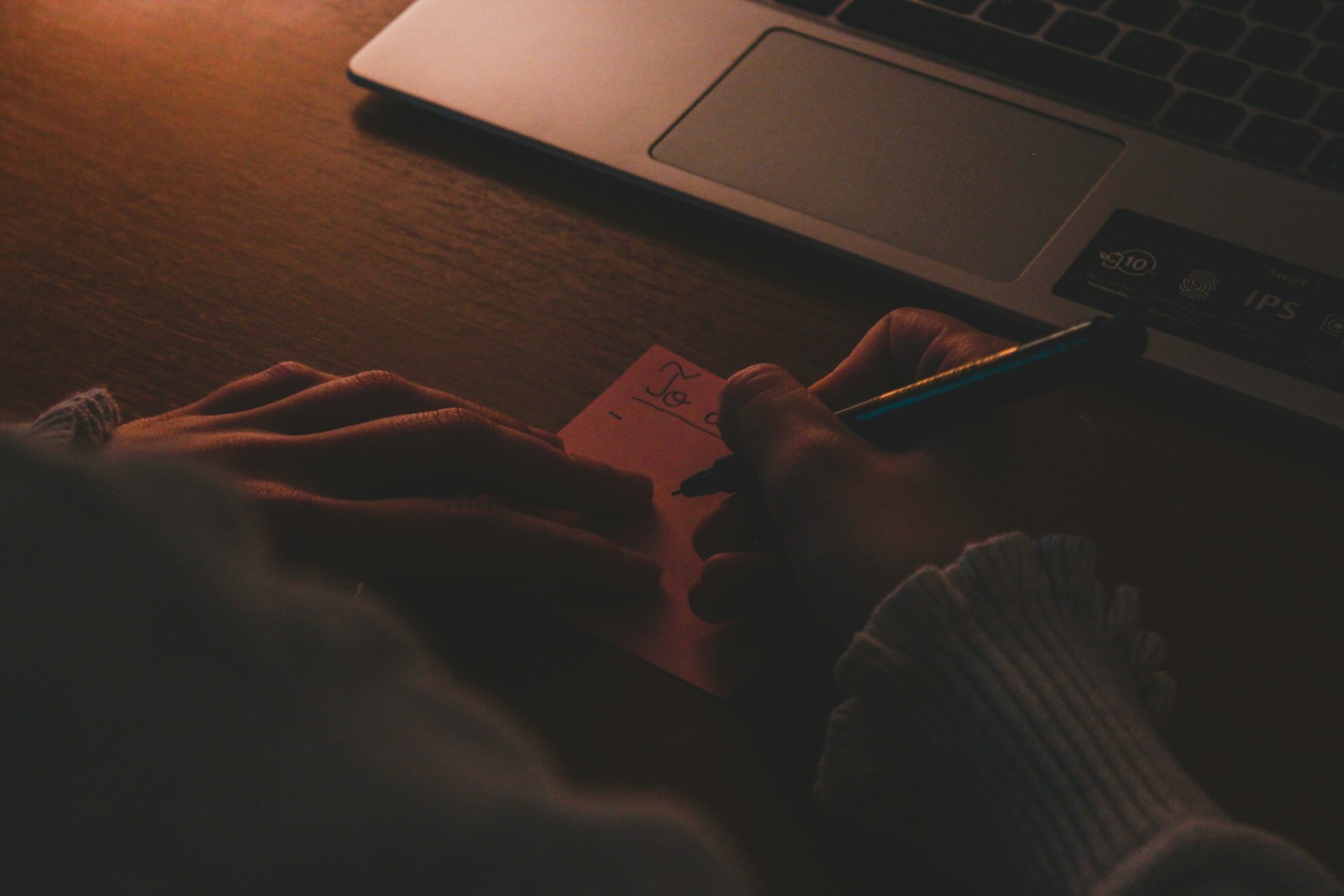 Mani che scrivono lista to-do su post-it accanto a laptop al buio con luce calda — i lavori sporchi ripetitivi che gli agenti AI possono togliere ai dipendenti